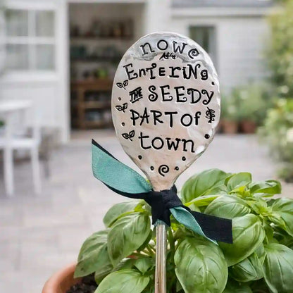 Decorative silver plate spoon with text  stuck in a plant in an outdoor setting