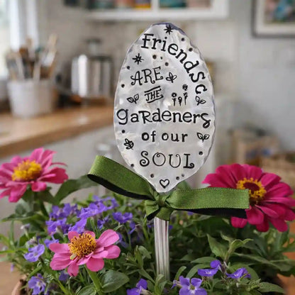Decorative spoon with a quote about friends in a garden setting with flowers.