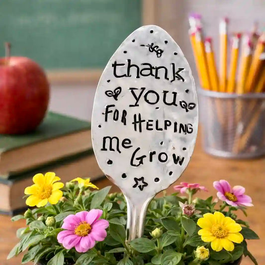 Silver spoon with 'thank you for helping me grow' text in a classroom setting with flowers and books.