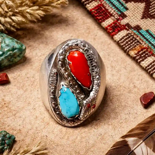 Silver ring with red and turquoise stones on a textured surface with natural elements.