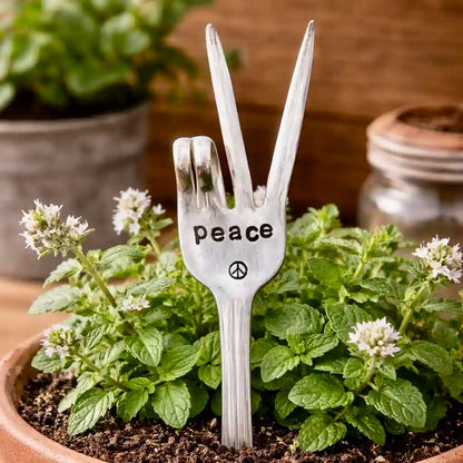 Silver fork with 'peace' engraved, standing in a pot of plants