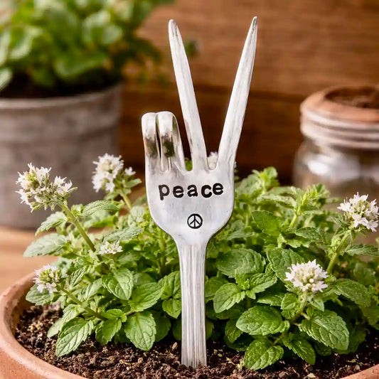 Silver fork with 'peace' engraved, standing in a pot of plants