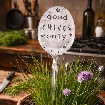 Decorative silver plate spoon with 'good chives only' text in a garden setting.