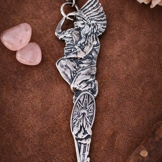 Silver Native American figure keychain on a brown surface with pink stones