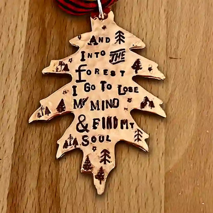 And Into The Forest I Go To Lose MY Mind & Find My Soul stamped into leaf-shaped copper ornament on wood background