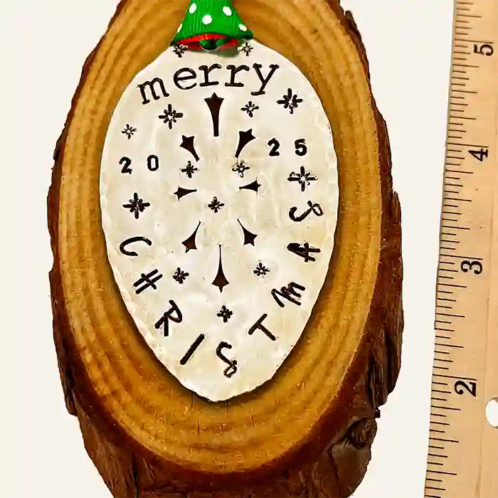 Vintage silver-plate slotted serving spoon with 2025 Christmas stamped on it, laying on piece of wood, measures 3 inches