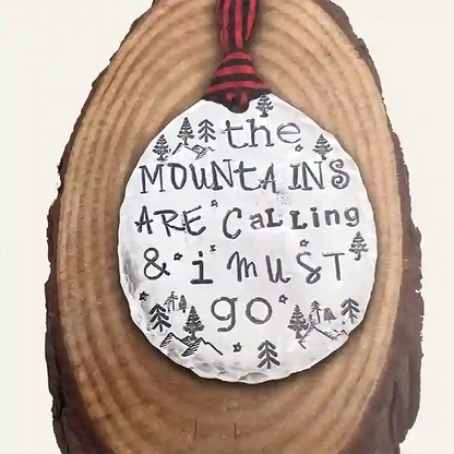 The Mountains Are Calling & I Must Go stamped into round vintage spoon ornament on wood background