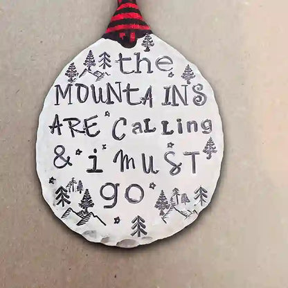 The Mountains Are Calling & I Must Go stamped into round vintage spoon making beautiful ornament on dark background