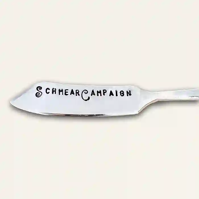 Silver butter knife with 'Schmear Campaign' text stamped on the spreader