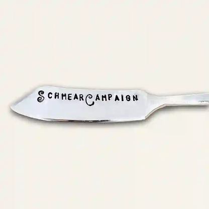 Silver butter knife with 'Schmear Campaign' text stamped on the spreader