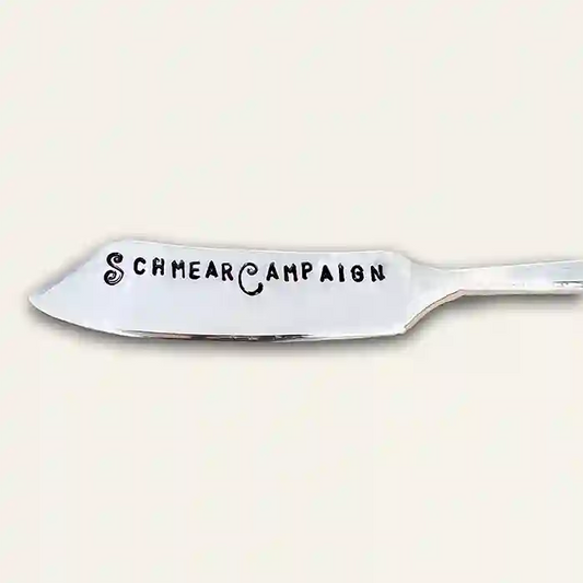 Silver butter knife with 'Schmear Campaign' text stamped on the spreader