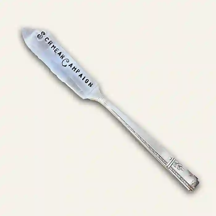 Silver butter knife with 'Schmear Campaign' text stamped on the spreader showing full image