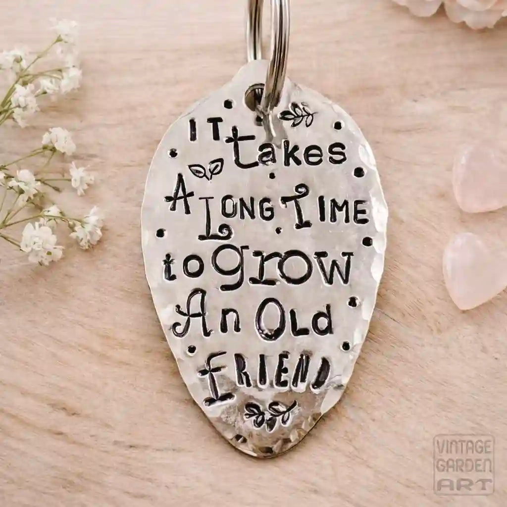 Silver keychain with engraved text on a wooden surface with flowers and stones.