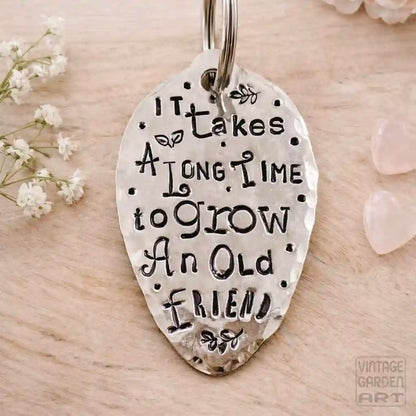Silver keychain with engraved text on a wooden surface with flowers and stones.
