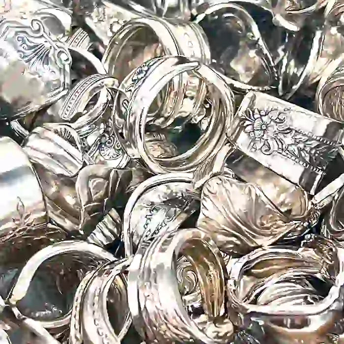A pile of handcrafted silverware spoon rings with classic detailed patterns on them.