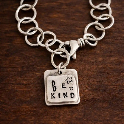 Silver chain necklace with 'BE KIND' pendant on a wooden surface