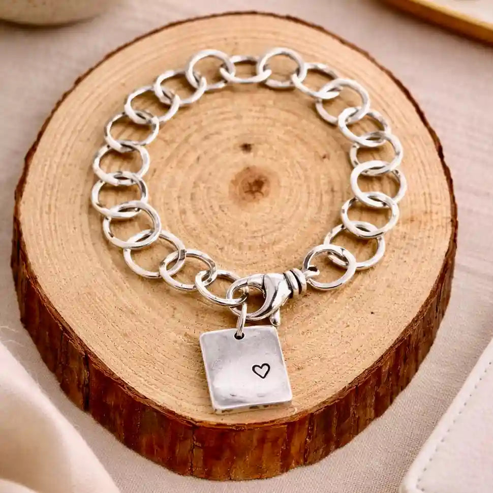 Silver chain bracelet with a heart charm on a wooden surface