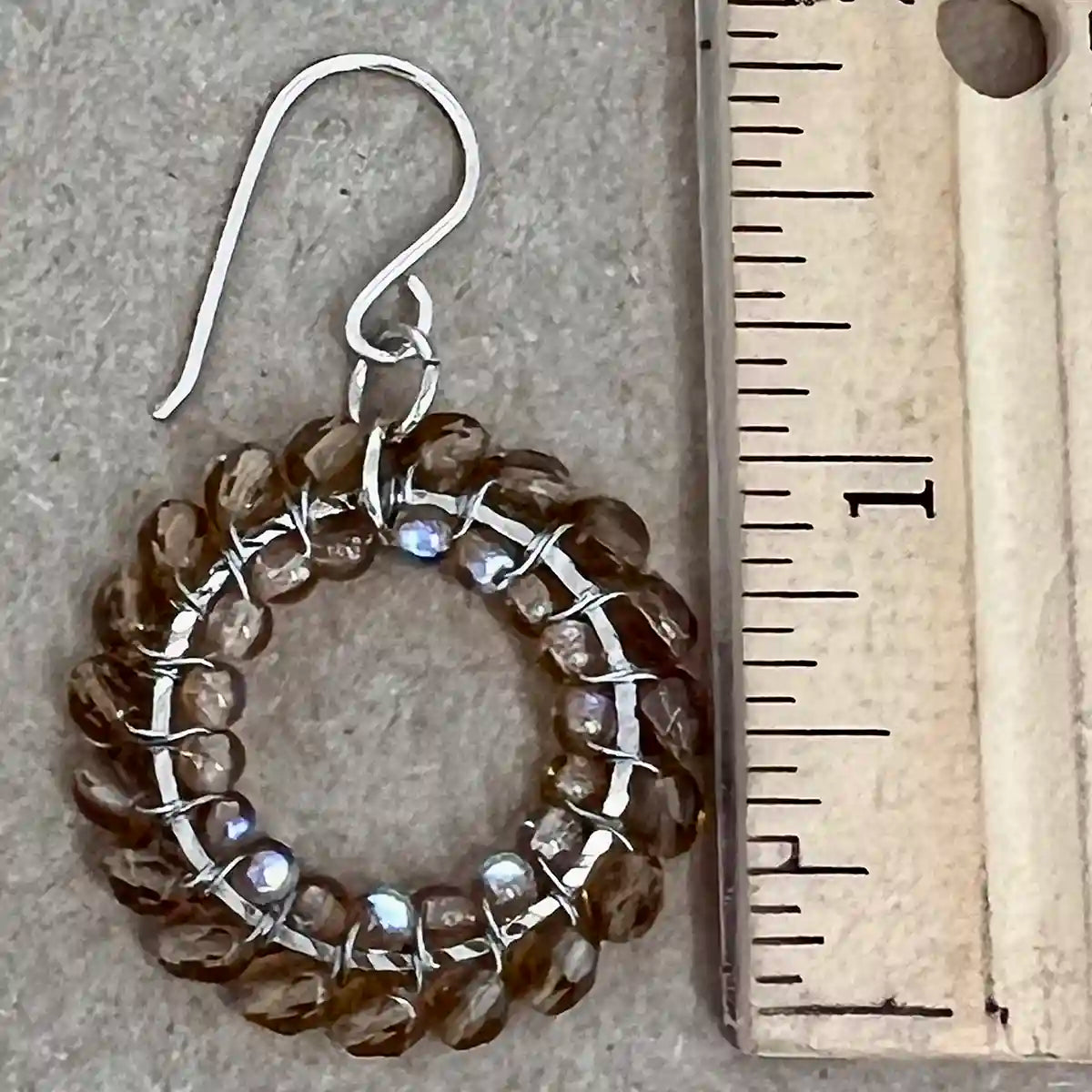 Silver earring with brown beads next to a ruler on a gray surface