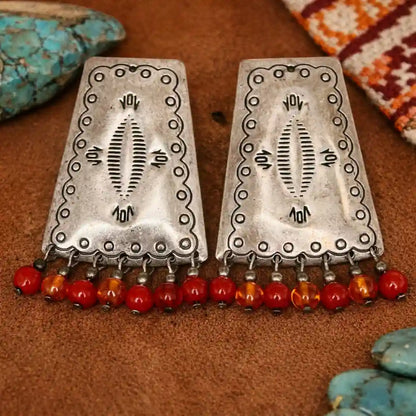 Pair of sterling silver southwest style earrings with red and orange beads on a brown surface