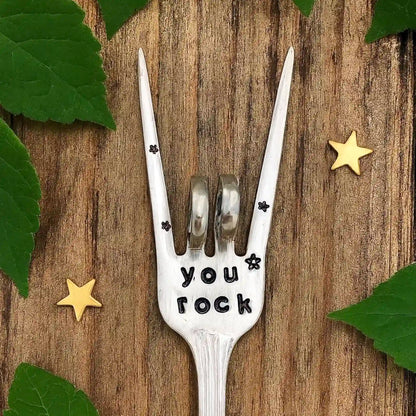 Silver fork with 'you rock' engraving on a wooden surface with leaves and stars.