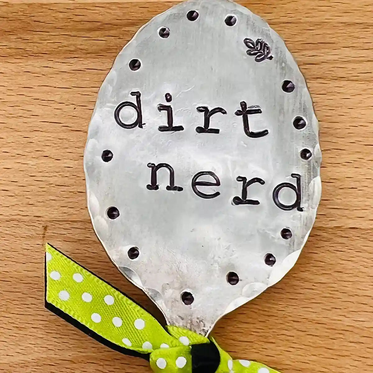 Silver plate spoon-shaped sign with 'dirt nerd' text on a wooden surface